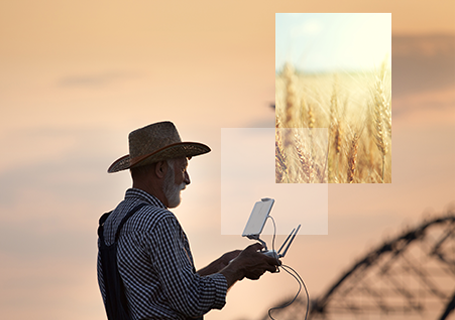 Old farmer with hat holding remote control for drone flying above field with irrigation system in summer