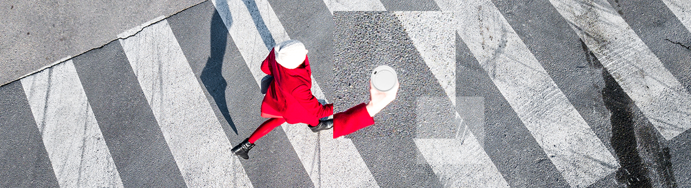 Aerial view of lady in red coat walking across a pedestrian crossing with a cup of coffee